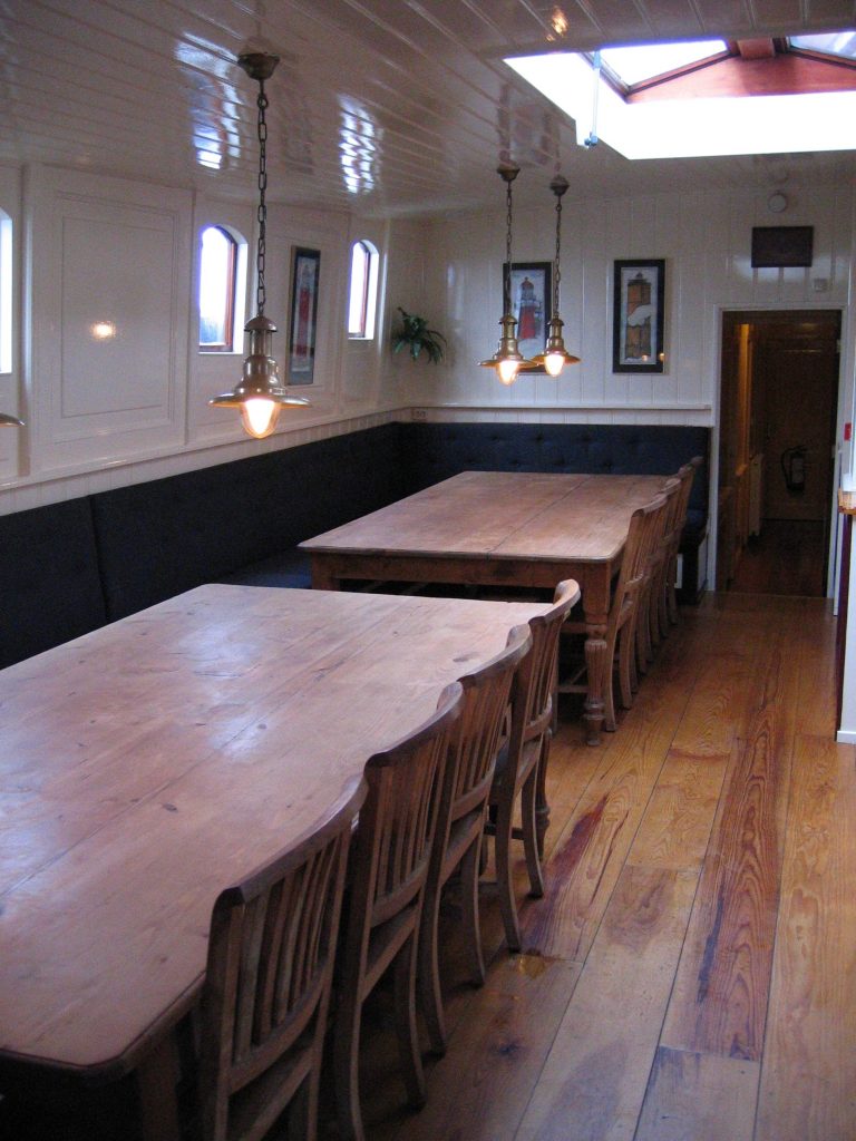 Twee lange houten tafels met houten stoelen in de eetzaal van het historische zeilschip Frans Horjus.