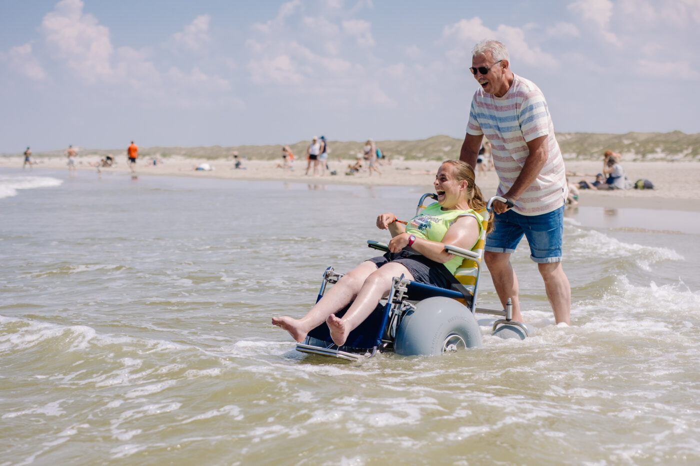 Een spastische vrouw en haar begeleider genieten van het zeewater in de Noordzee in een Strandrolstoel