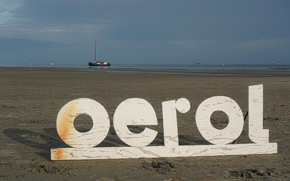 Stalen letters die het woord Oerol vormen weerspiegelen het strand op de Noordsvaarder met op de achtergrond een drooggevallen schip op het Wad.