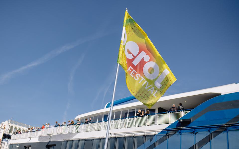 Een geel-rode Oerol-vlag wappert terwijl veerboot Willem de Vlamingh aanlegt in de haven van Terschelling.