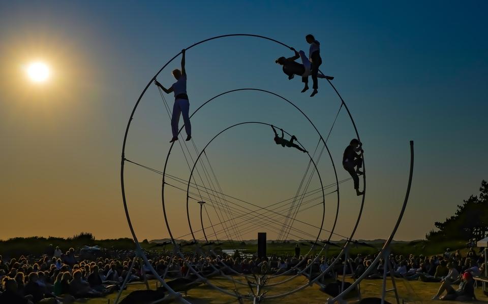 Vijf vrouwelijke acrobaten hangen aan een grote stalen spiraal van theatergezelschap Rhizome tijdens de voorstelling La Spire bij het licht van de ondergaande zin tijdens Oerol 2023.