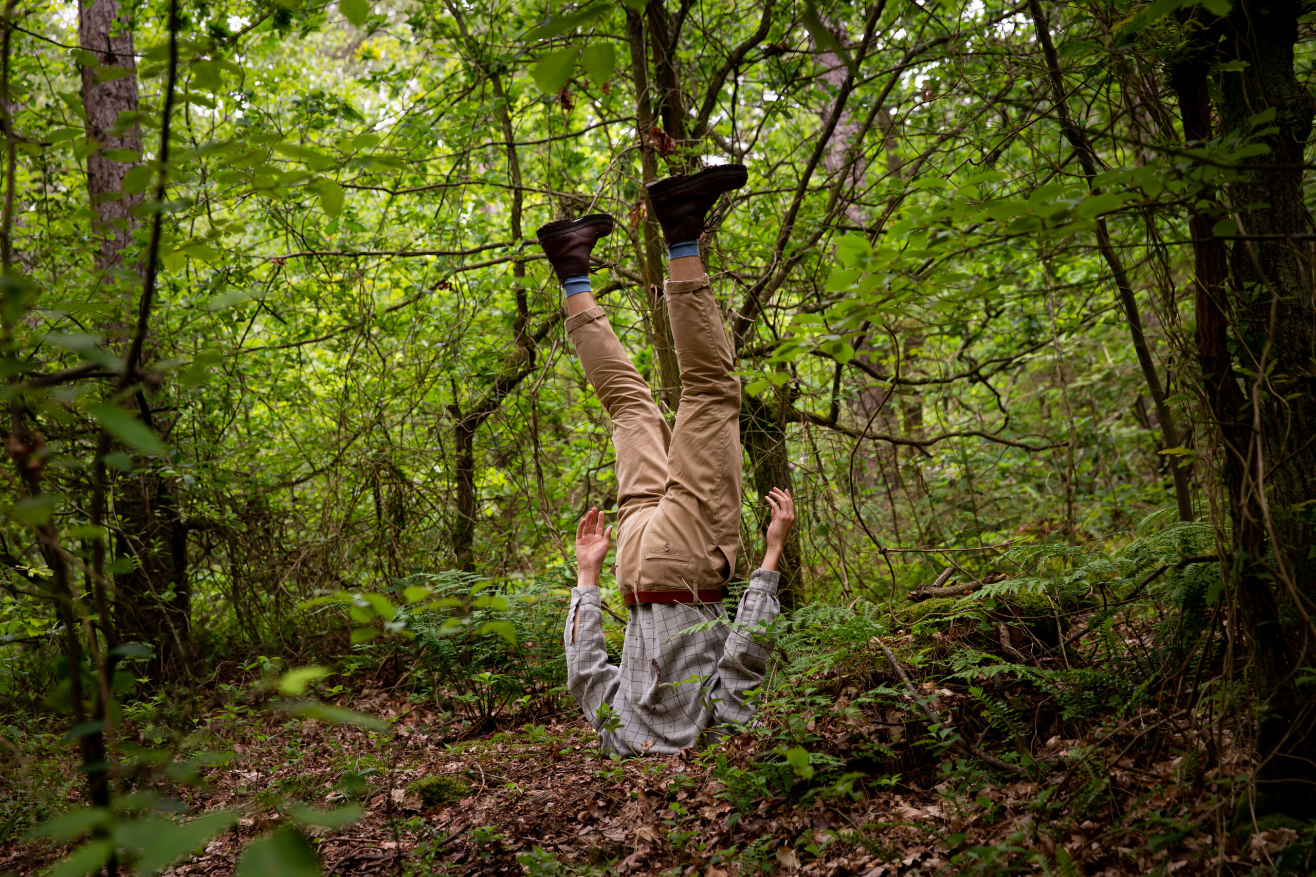 Een man staat op zijn kop, met zijn hoofd ingegraven, in het bos tijdens de Atelierroute van Oerol in 2019.