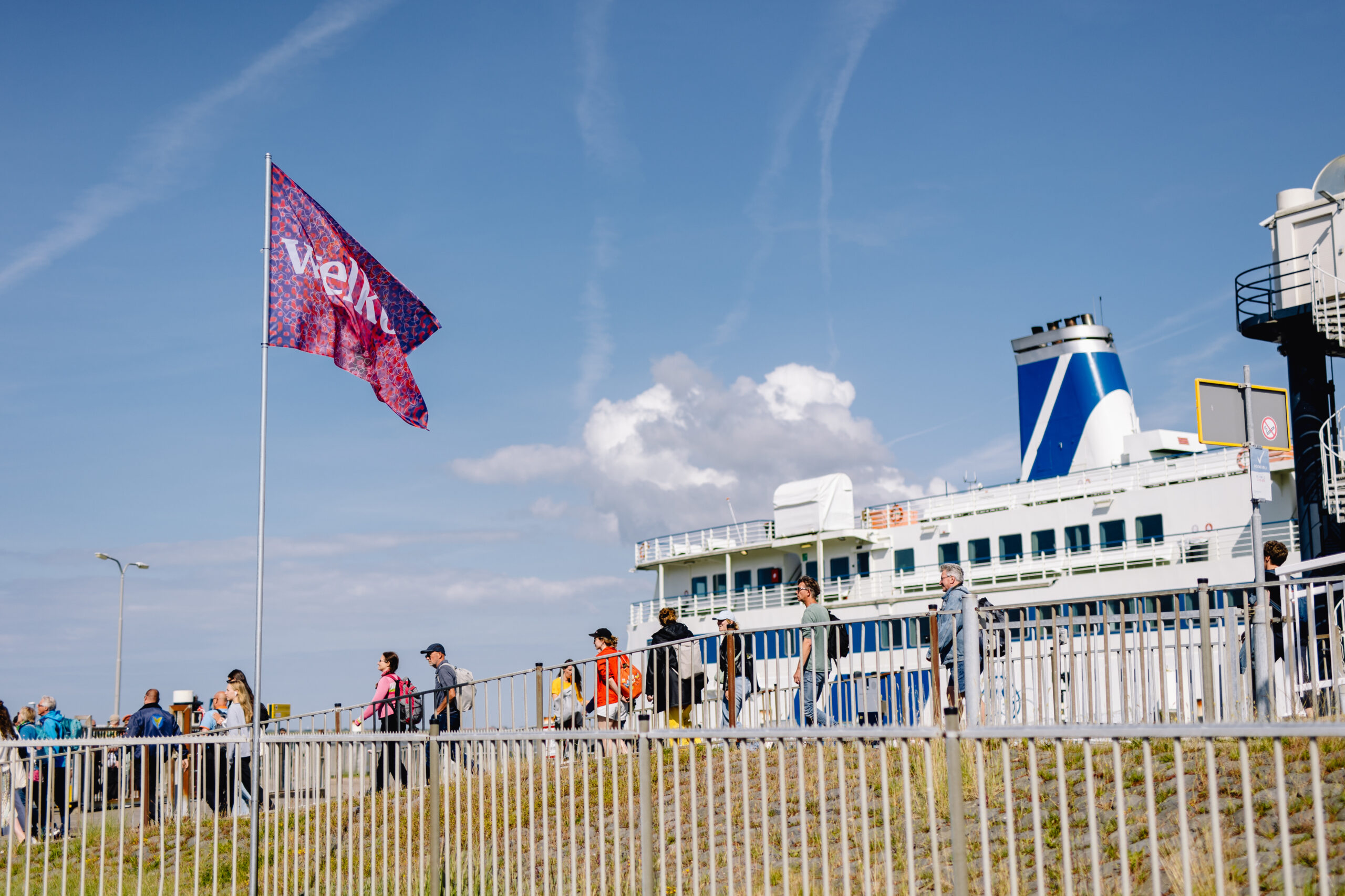 Oerol vlag wappert boven bezoekers die van de boot van Rederij Doeksen Terschelling op wandelen.