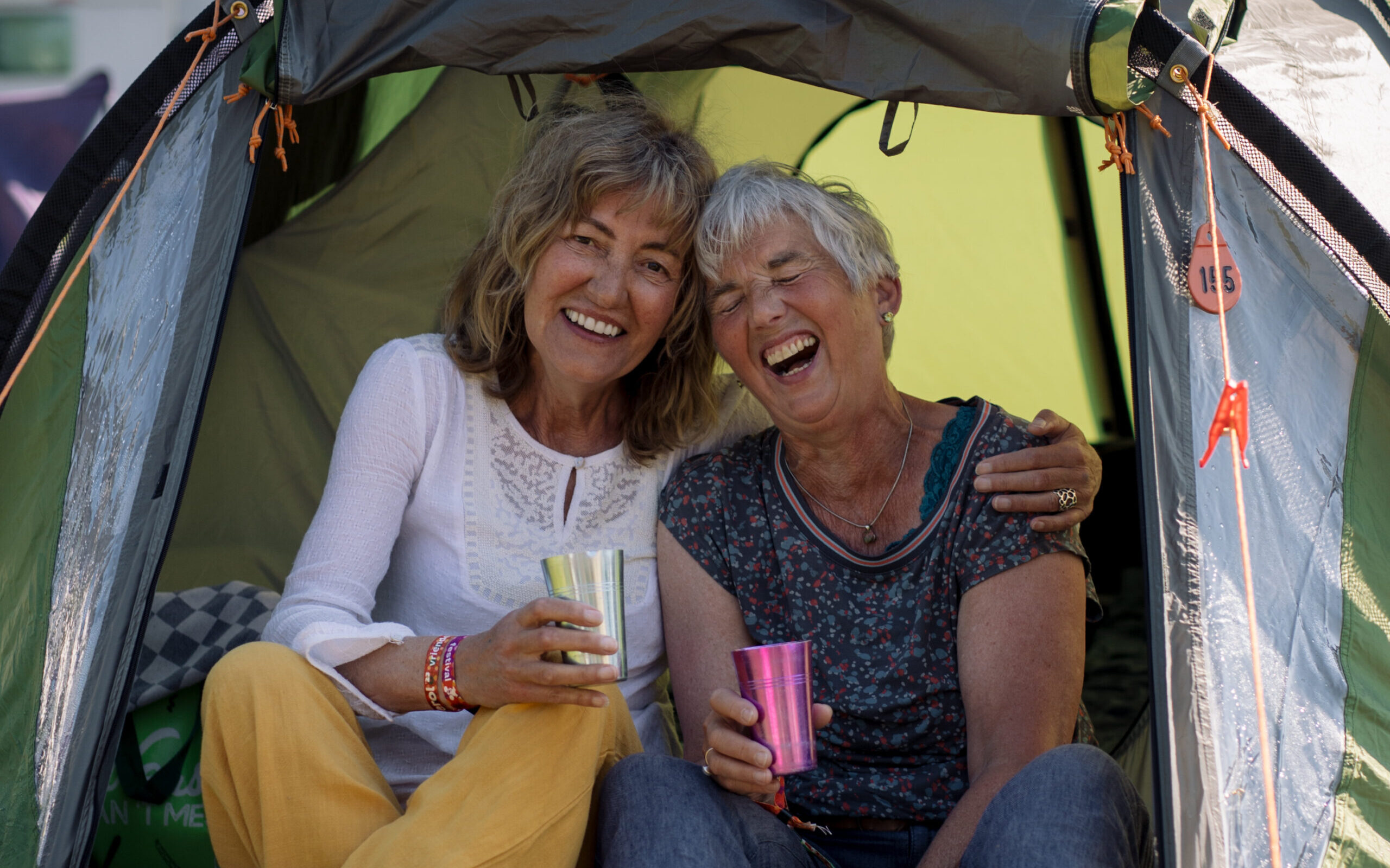 Twee vijftigplus vriendinnen aan de koffie in de deuropening van hun tent