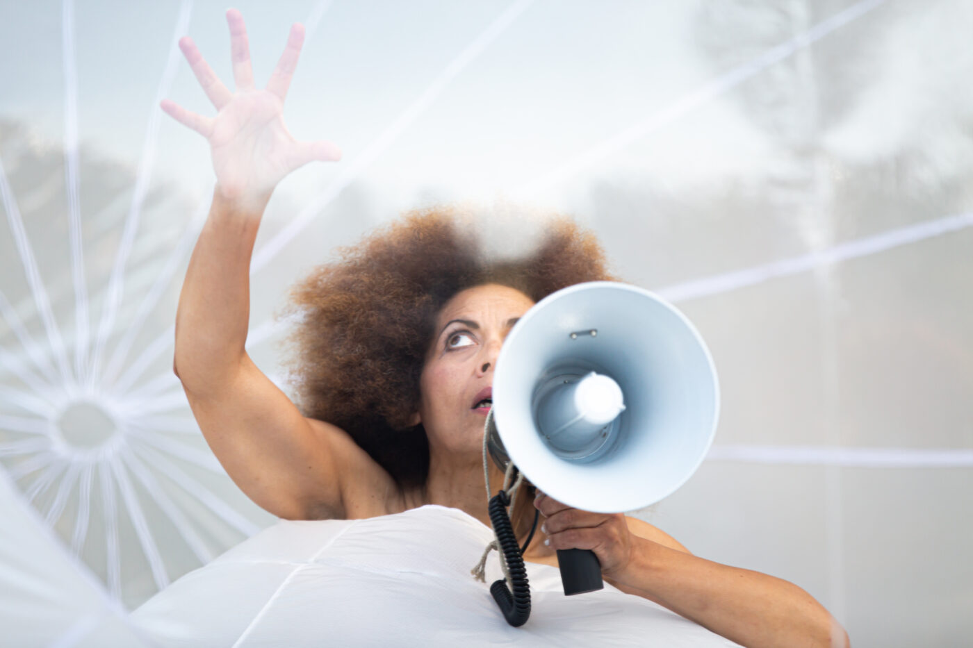 Vrouw met een witte megafoon kijkt bezorgd omhoog, beeld uit theatervoorstelling Stay Out van collectief Plastique Fantastique, Oerol 2022.