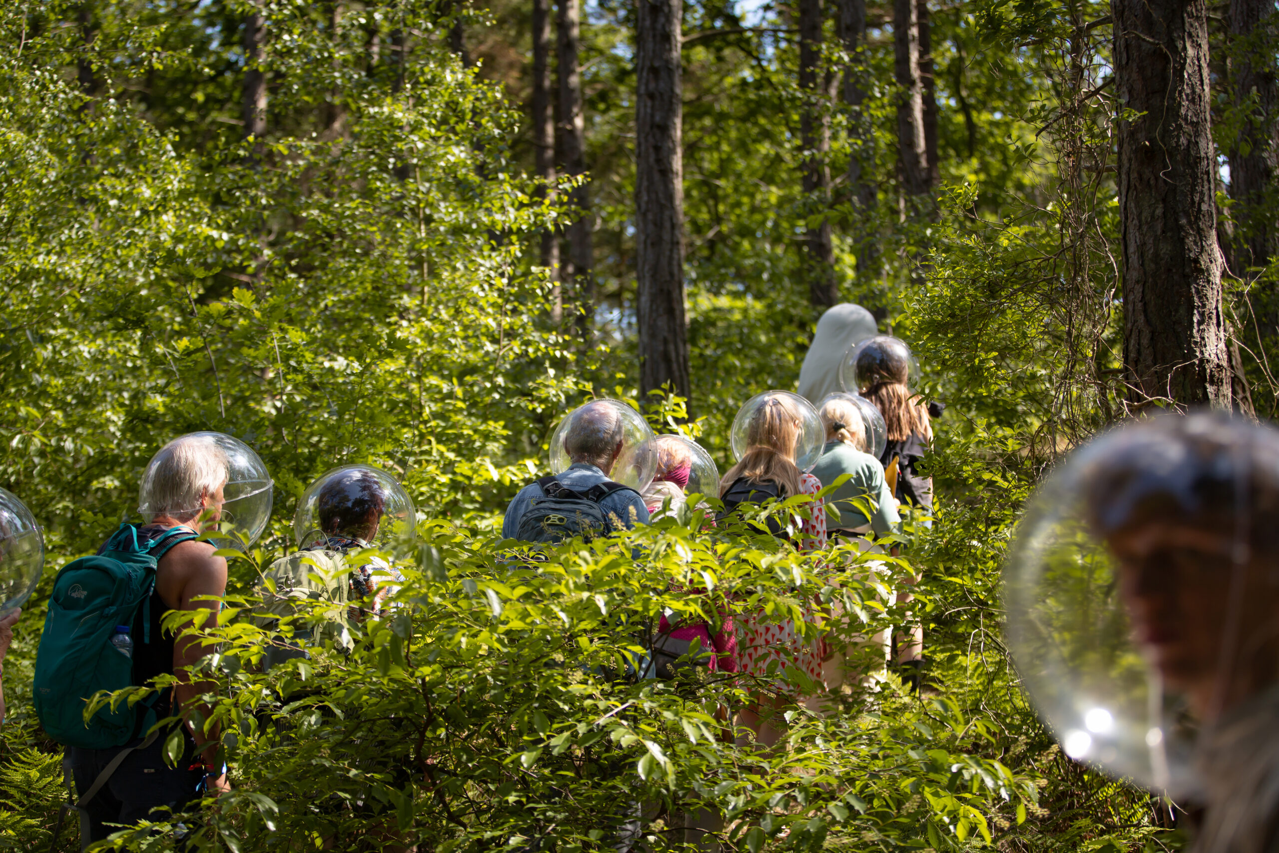 mensen lopen door het bos met transparante bollen op hun hoofd tijdens theatervoorstelling Stay Out van Plastique Fantastique tijdens Oerol 2022.