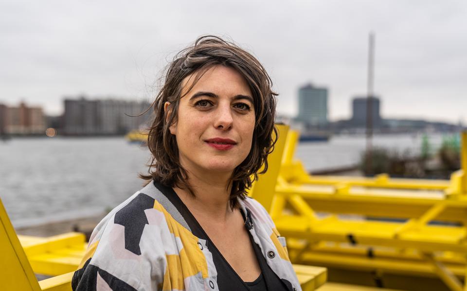 Portret van Artistiek leider van Oerol Sabine Pater met op de achtergrond kleurrijke gele banken en de skyline van Amsterdam.