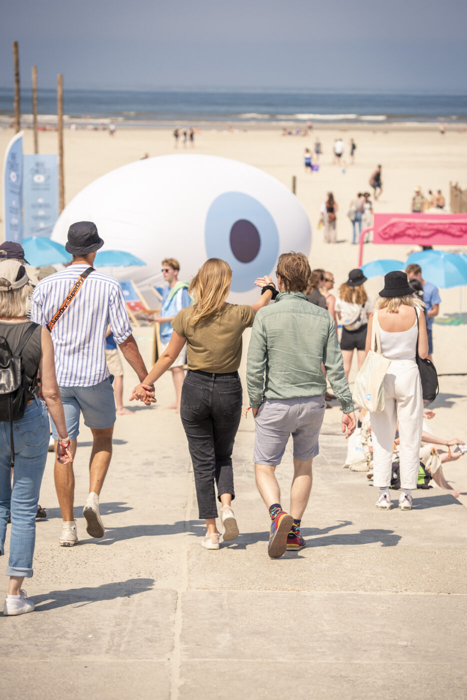 Mensen lopen het strand op met op de achtergrond een opblaasoog, beeldmerk van de Wie checkt jou campagne van KNRM Nederland tijdens Oerol 2023
