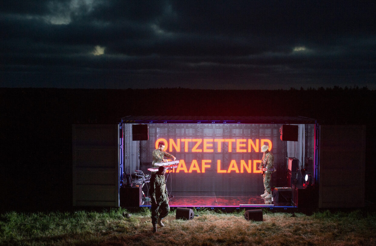 Rapper Sef staat voor een scherm waarop staat Ontzettend gaaf land, voorstellingsbeeld uit theatervoorstelling Vlag van Likeminds gespeeld tijdens Oerol 2023