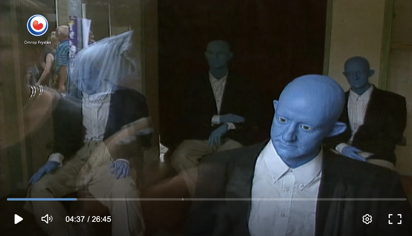 Still van de compilatievideo van Oerol 1997, waarop mannen in pak met blauwe hoofden te zien zijn achter een winkelruit
