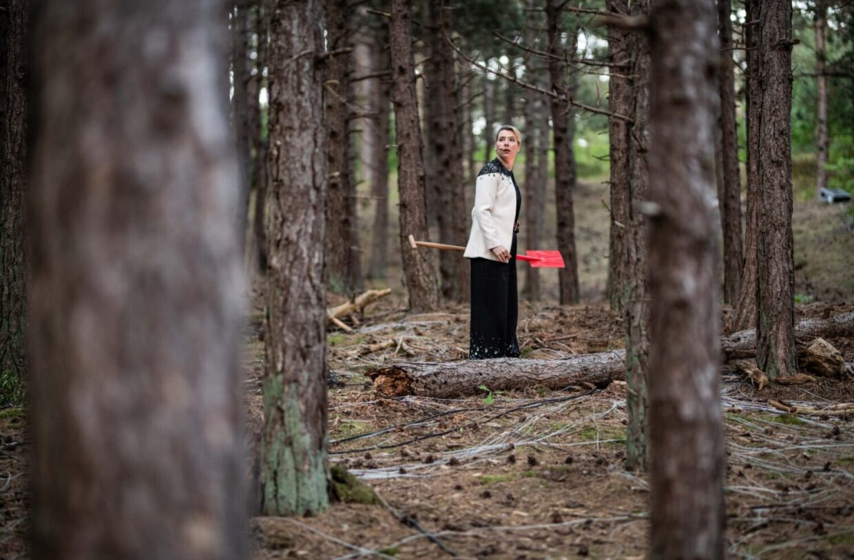 Vrouw staat met rode schep in het bos, voorstellingsbeeld uit We Moeten Iets Met Het Landje van theatergroep Suburbia, gespeeld tijdens Oerol 2023